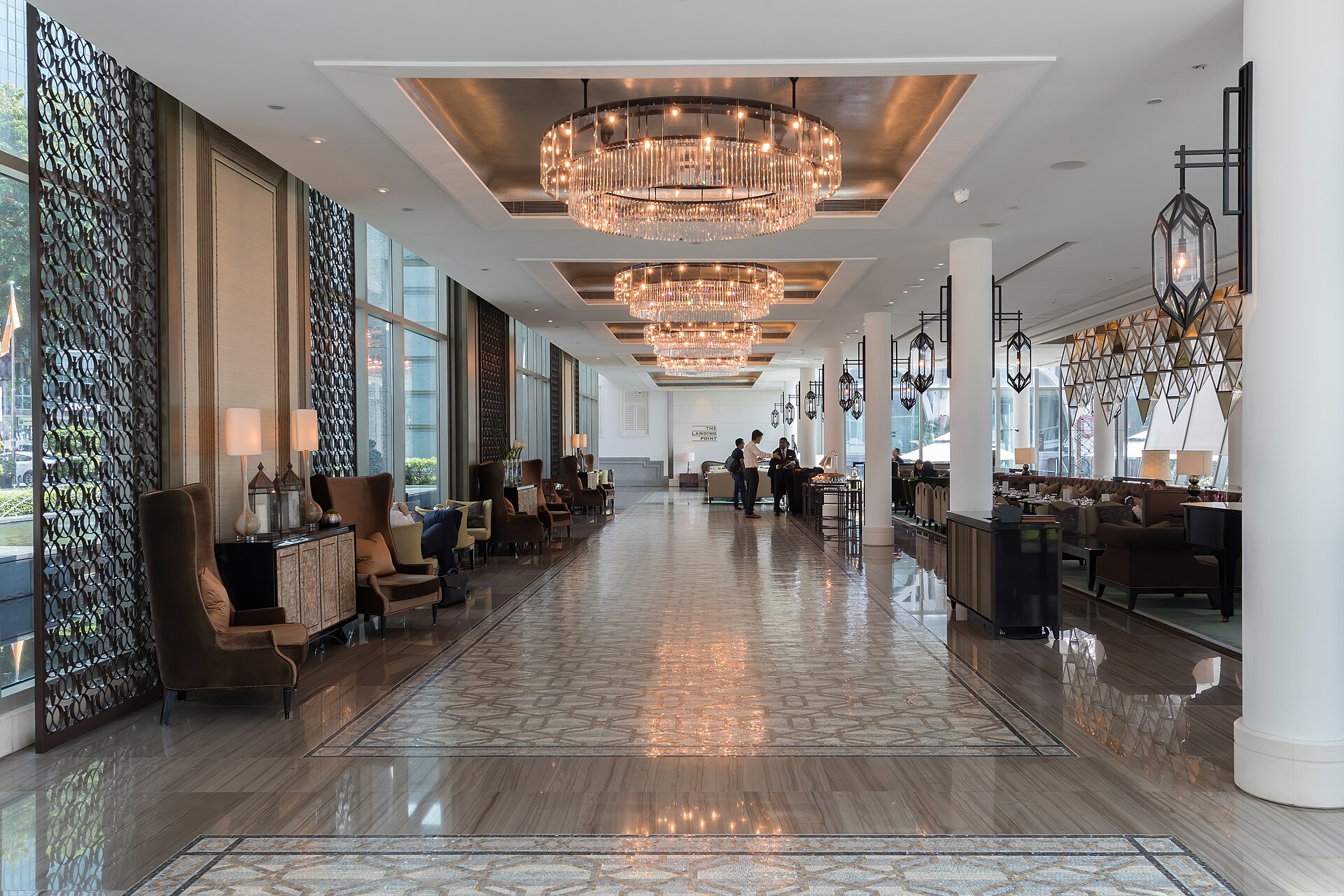 Interior lobi hotel luas dengan deretan lampu gantung dan area duduk, sebagai referensi suasana hospitality